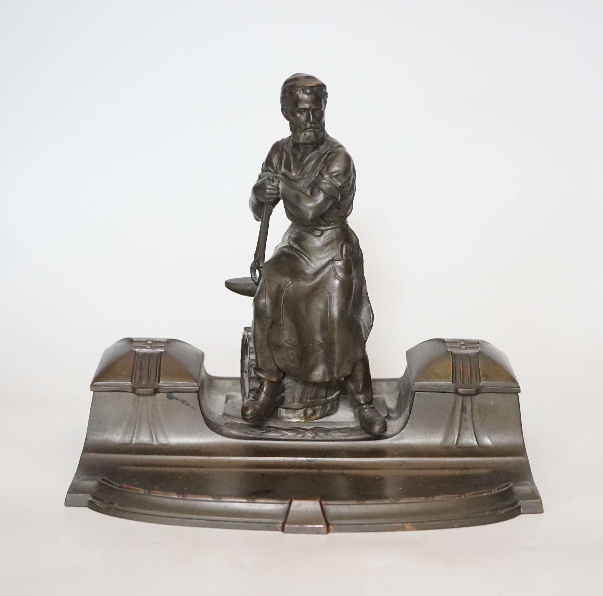 A WMF style spelter ‘Industry’ inkstand, figure with tools and an anvil, hinged ink wells either side, one glass ink bottle present, ‘1265’ cast into base, 20cm high